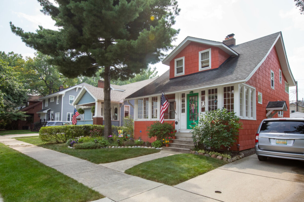 A red-shingled house on a quiet block, with a green door and a front walk.