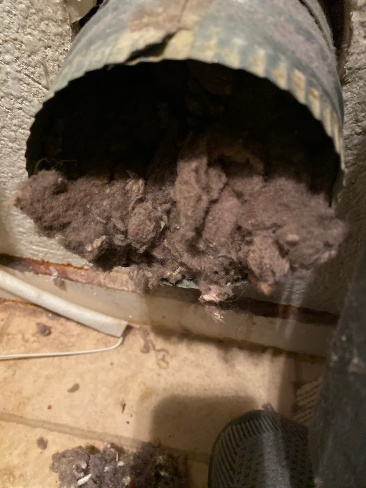 A metal dryer duct packed with gray lint where it meets the wall.