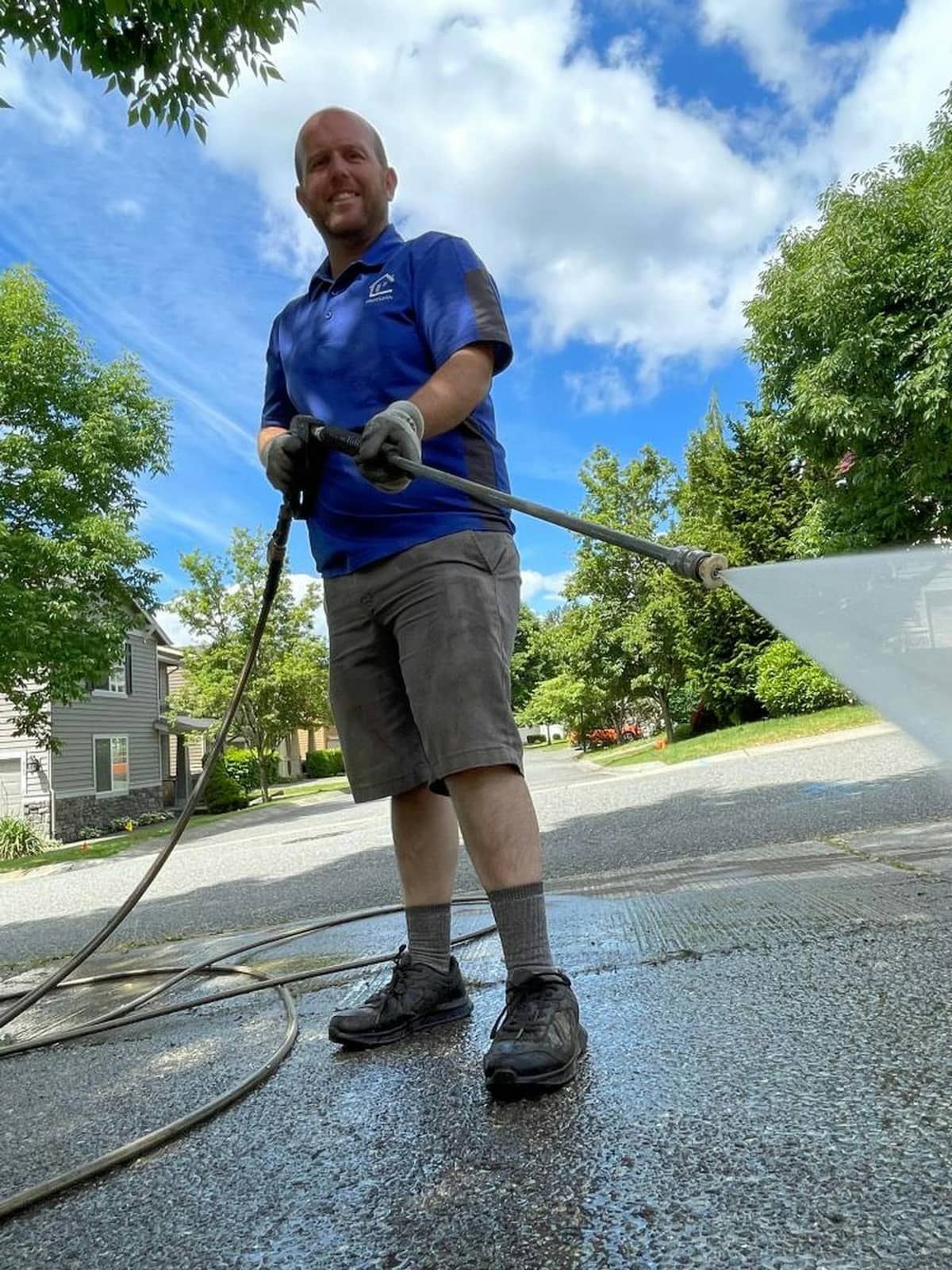 A man pressure washing a concrete driveway on a residential street.