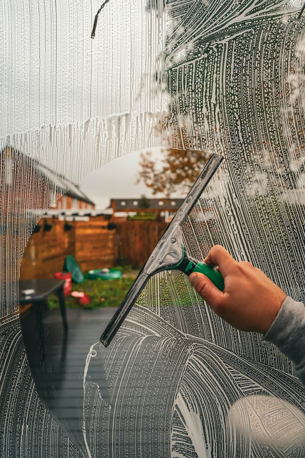 A hand drawing a squeegee through soapy water on a window pane.