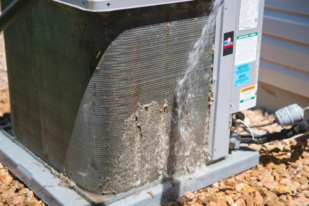 An outdoor air conditioner condenser with dirt and debris caked into its fins.