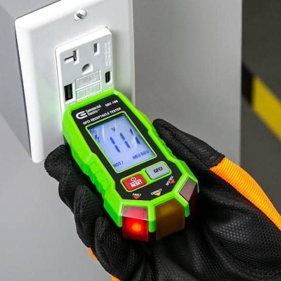 A gloved hand holding an outlet tester plugged into a GFCI outlet.