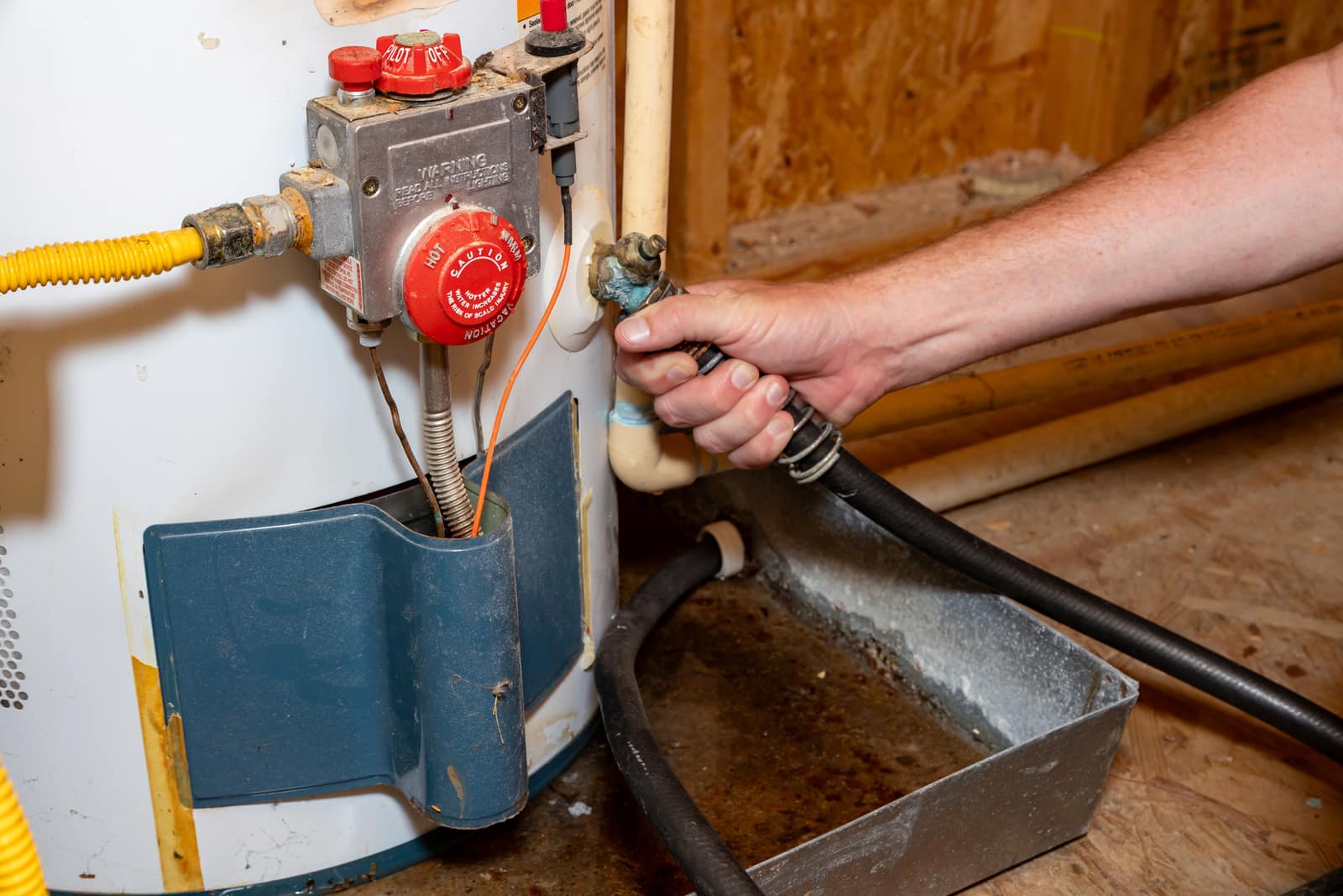 A hose attached to the drain valve of a gas water heater, draining into a pan.