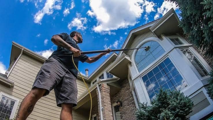 A man cleaning the upper windows of a two-story house with a long water-fed pole.