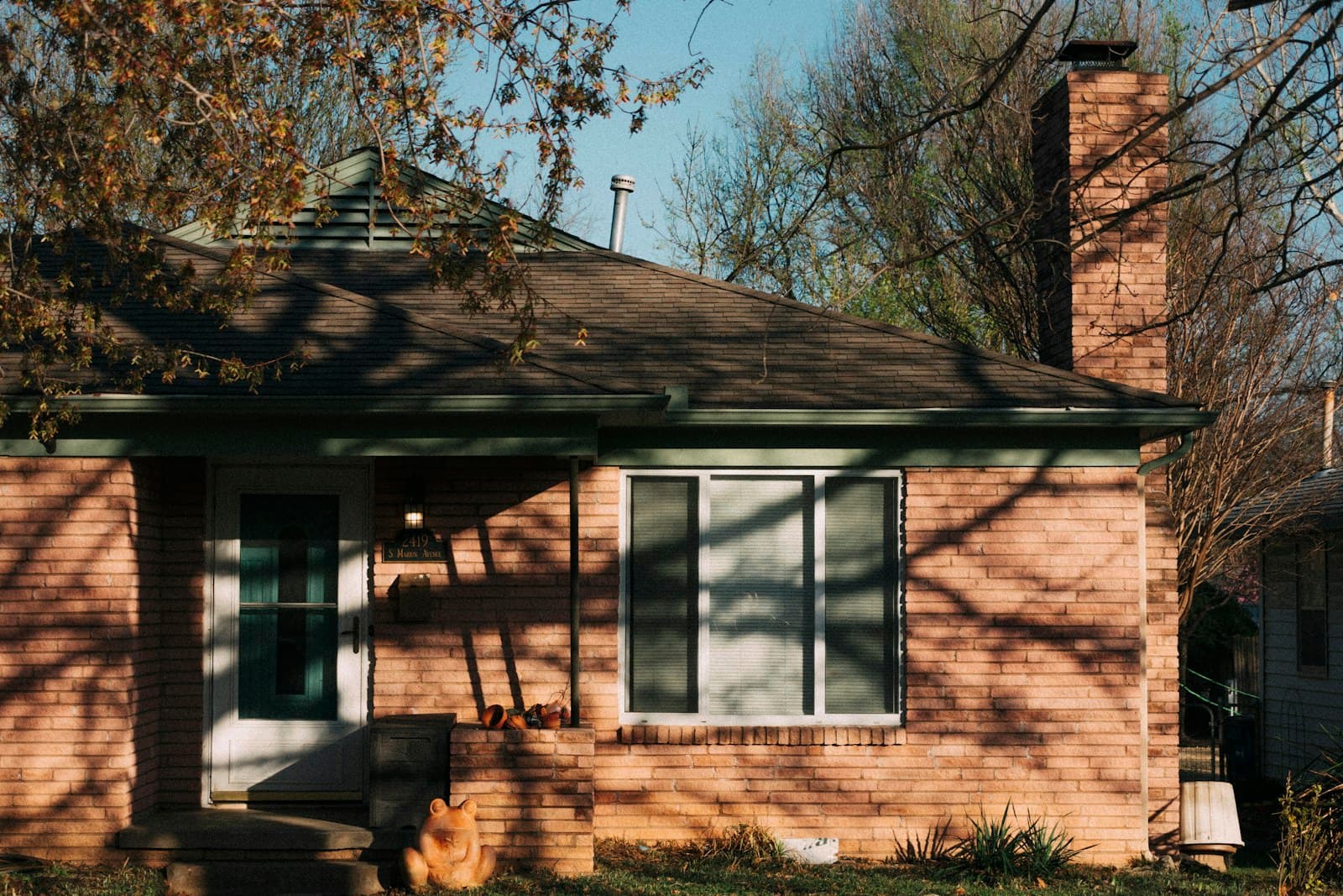A small brick bungalow with a picture window and a tall chimney in afternoon light.