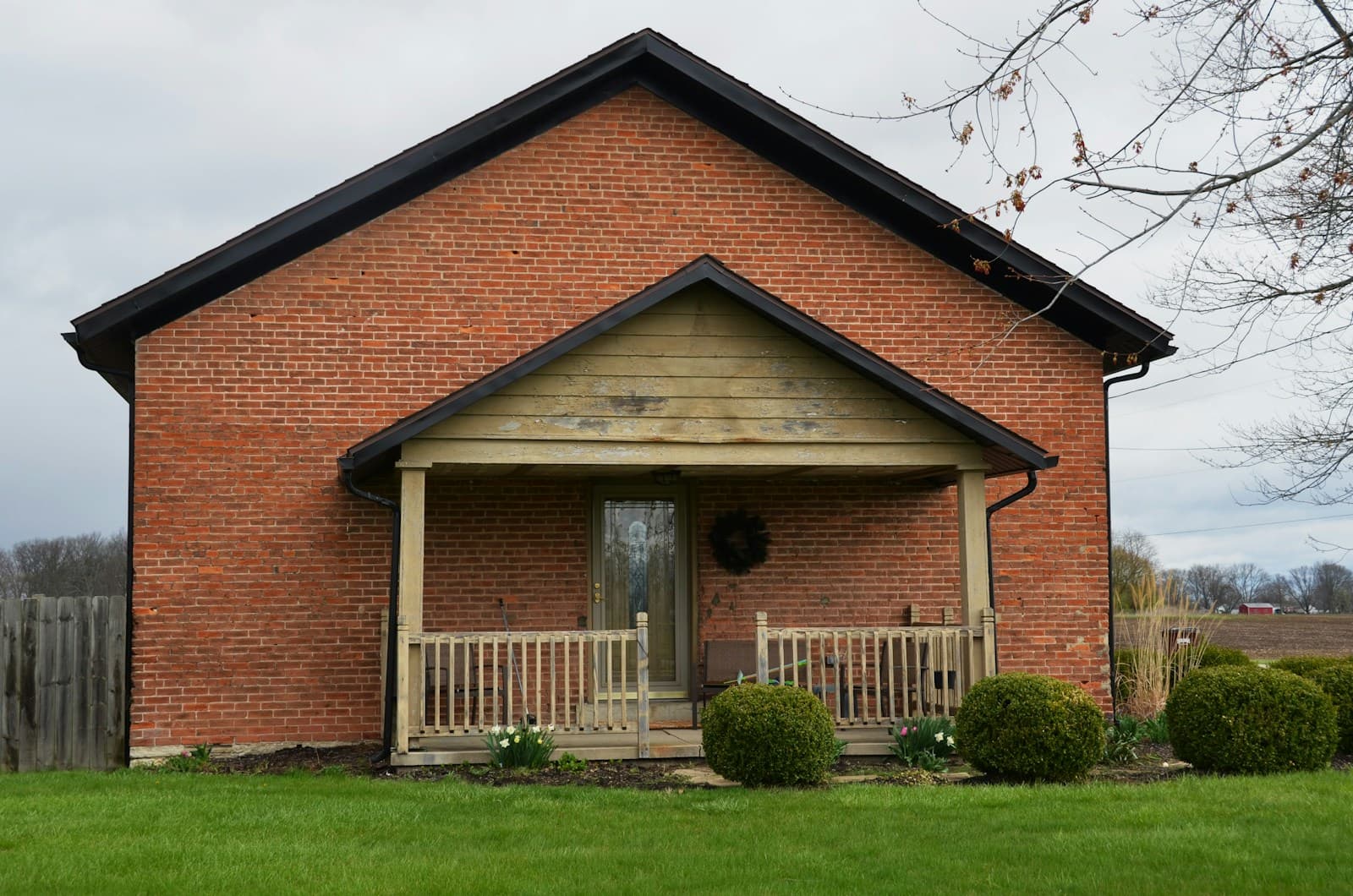 A small brick house with a gabled front porch and a wreath on the door.