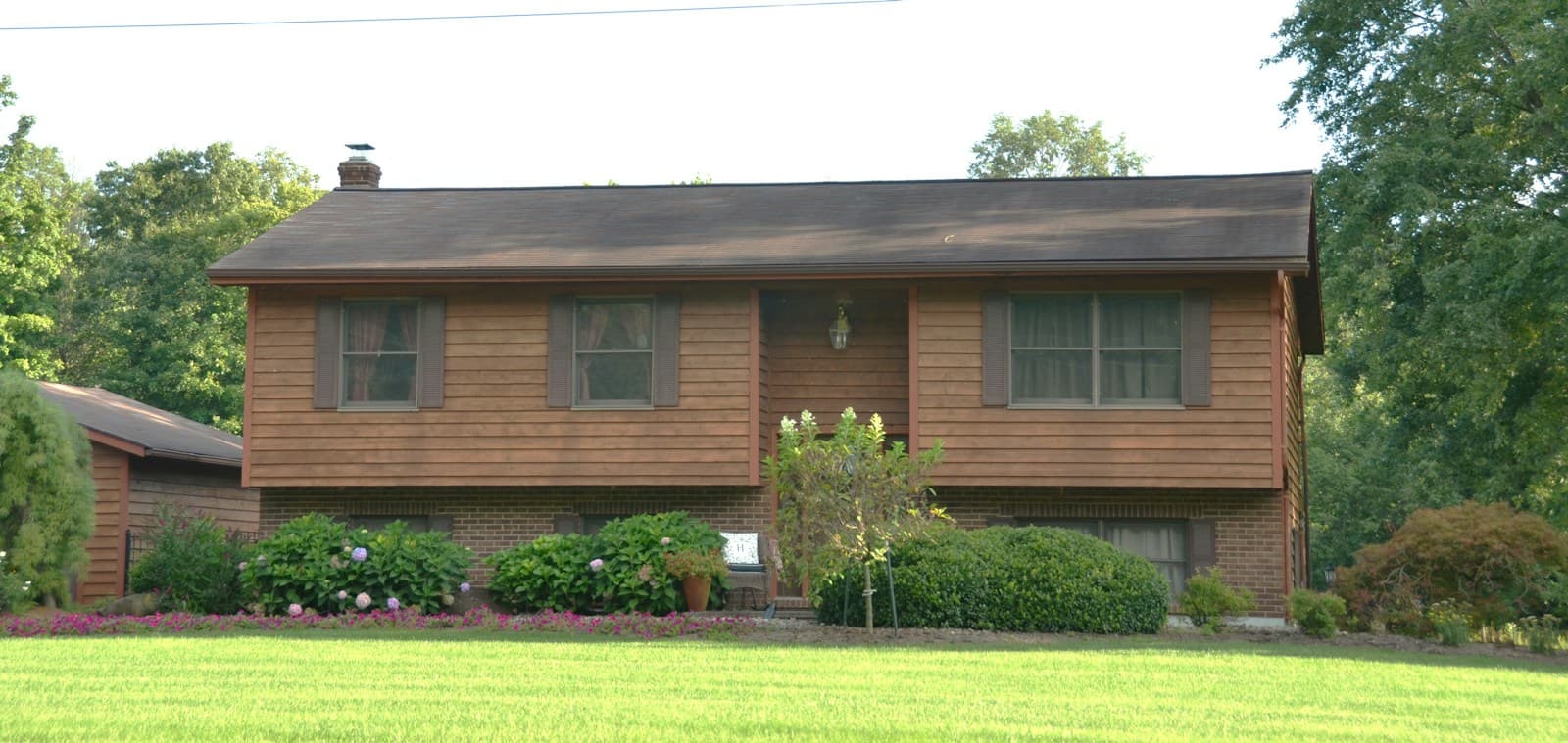 A split-level house with a brick lower story and wood siding above, on a wide lawn.