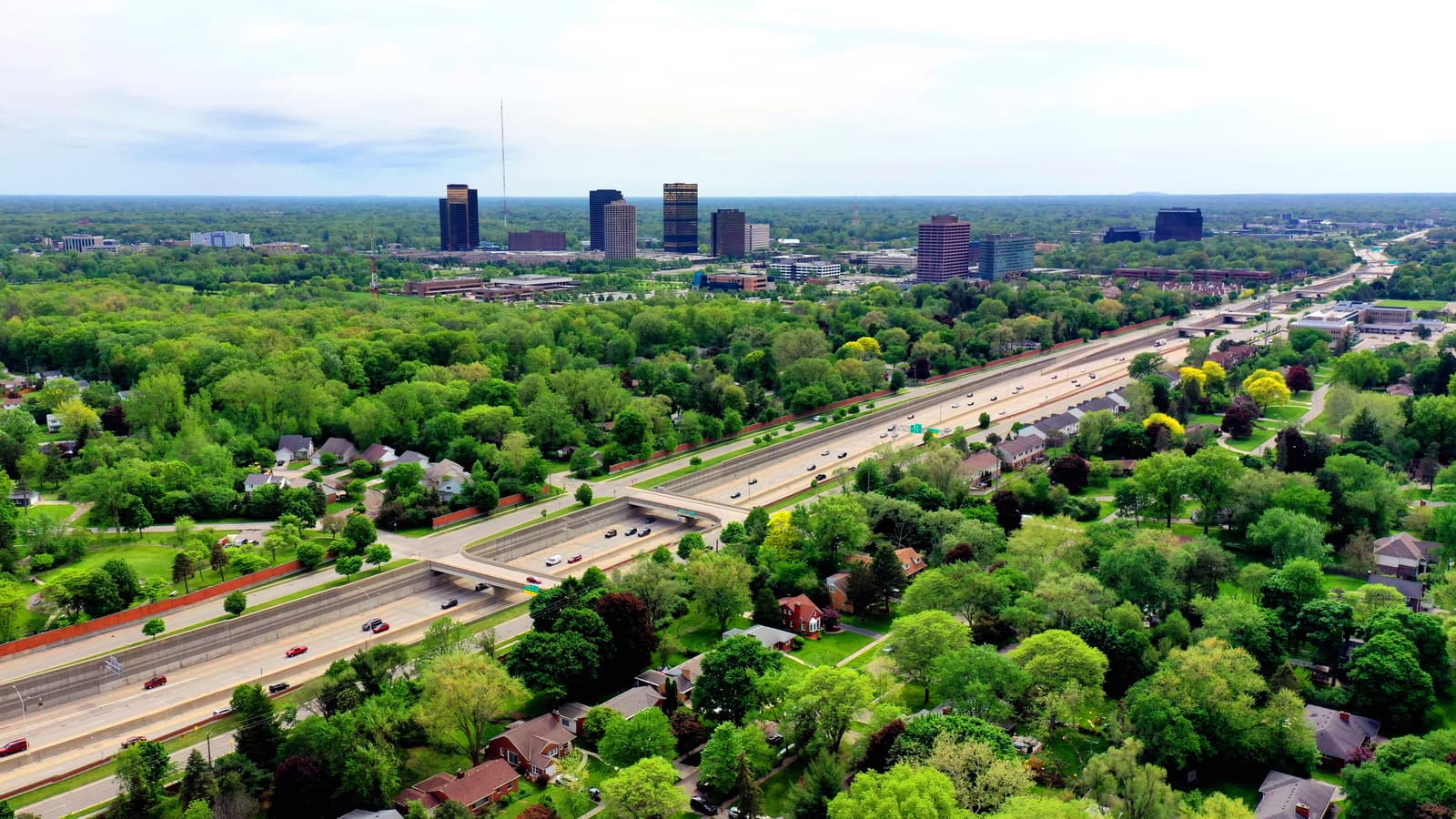 An aerial view of Southfield, Michigan, with the Southfield Town Center towers beyond a tree canopy and a freeway.